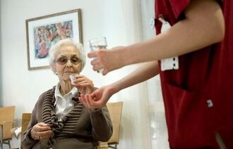 Bildet viser en eldre kvinne som får utdelt medisiner