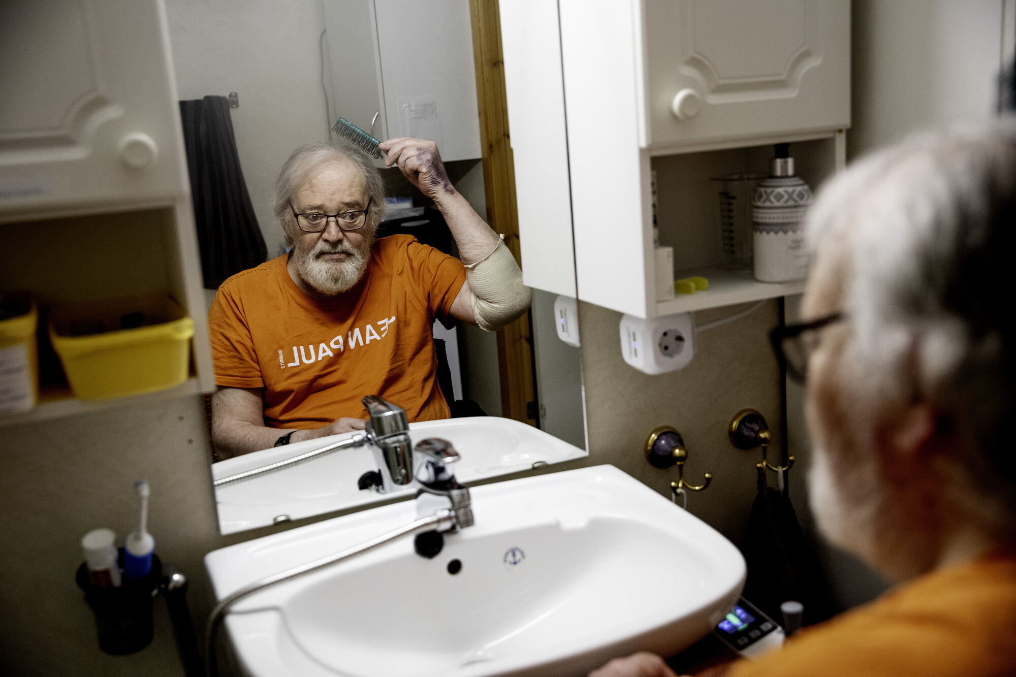 Bilde av eldre mann som grer håret foran speil.