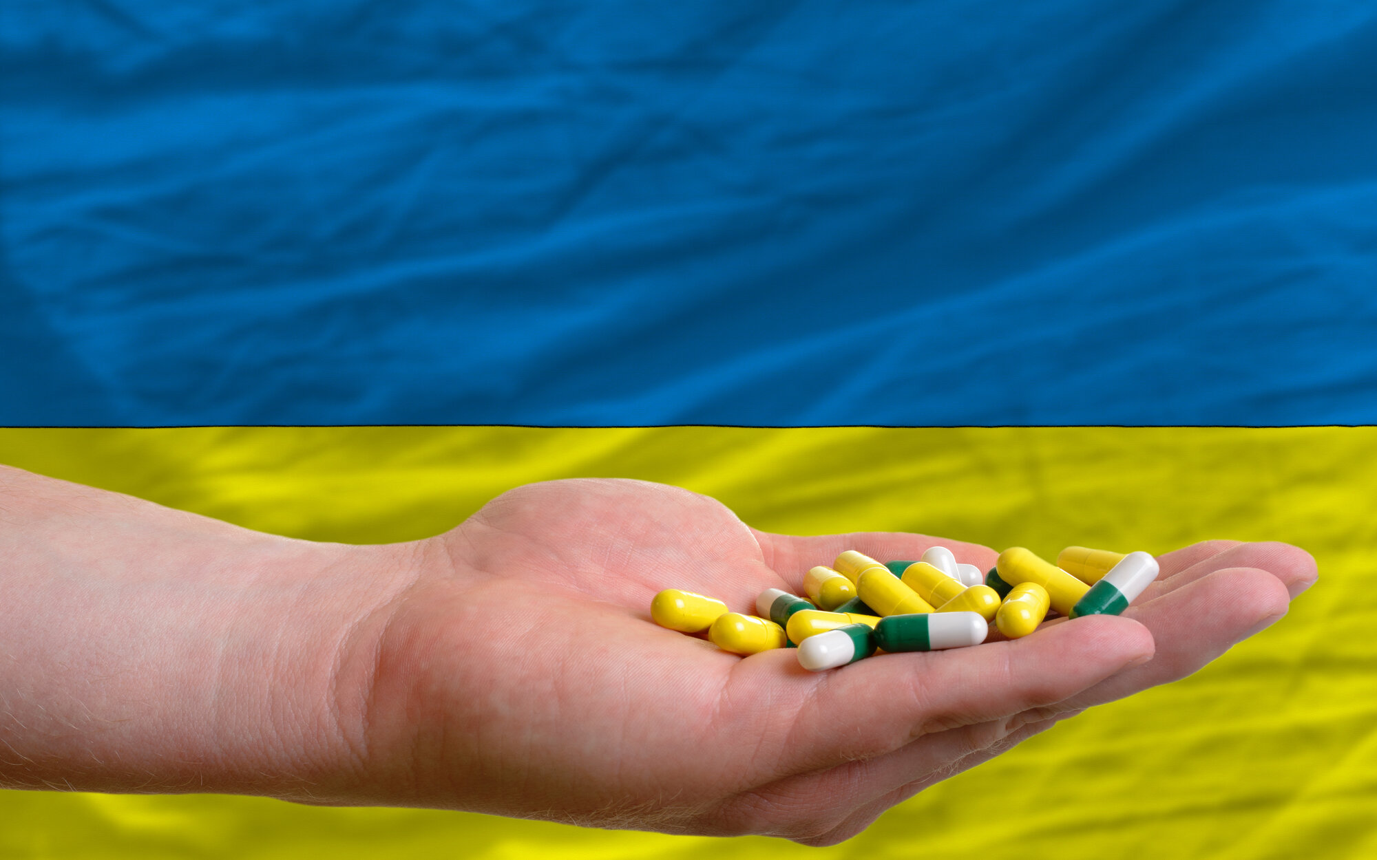 Bildet viser en hånd som holder piller, i bakgrunnen ses litt av det ukrainske flagget.