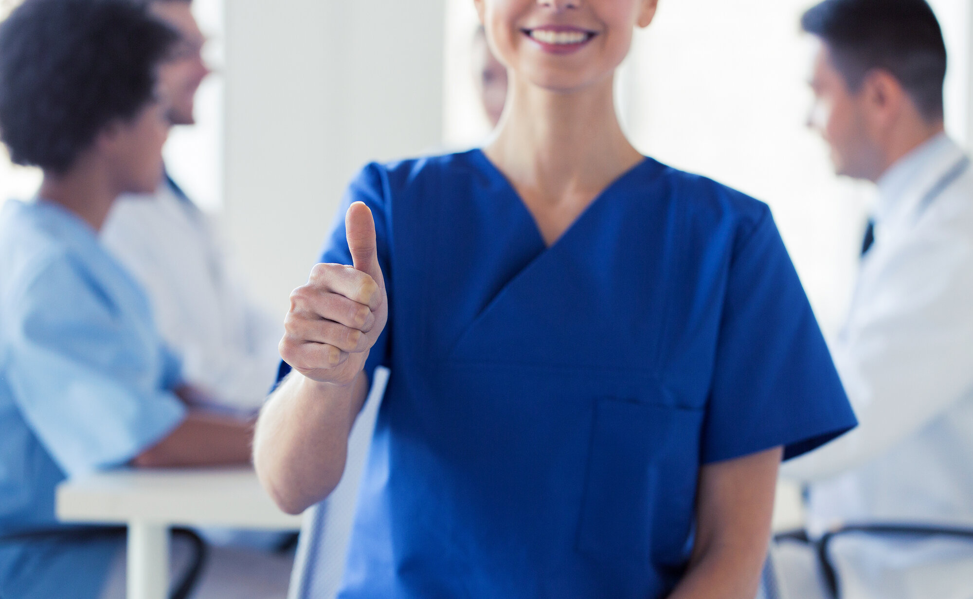 Bildet viser en sykepleier i front som viser "tommel opp" mens hun smiler.