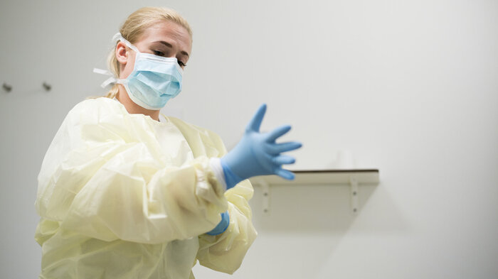 Bildet viser sykepleier Silvia Lopez, kledd i gul smittedrakt, som tar på seg hansker