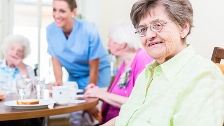 Fornøyde eldre på sykehjem med ansatt i bakgrunnen