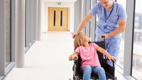 En mannlig sykepleier sammen med et barn i rullestol