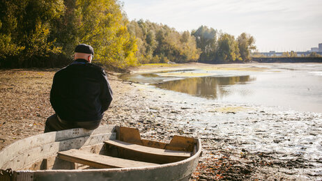Bildet viser en mann som sitter på en båt og ser ut over en innsjø