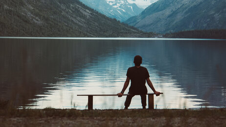 Bildet viser en mann som sitter alene på en benk og ser utover fjorden