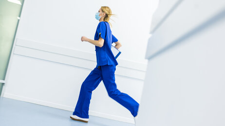 Bildet viser en sykepleier med munnbind som løper i korridoren