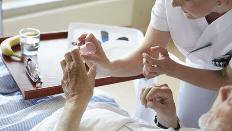 Bildet viser en kvinnelig sykepleier som gir en sengeliggende pasient medisin.