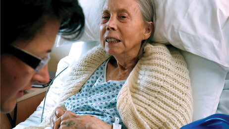 Bilde viser pleier hos en eldre dame som ligger i sengen.