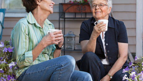 To eldre kvinner tar en kopp te i hagen