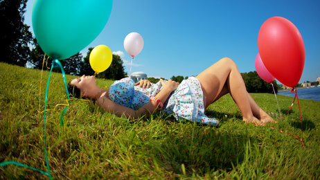 Bildet viser en gravid kvinne liggende i en eng med ballonger rundt omkring.