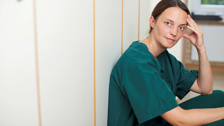 Bildet viser en sykepleier som sitter i en gang og ser tankefull ut
