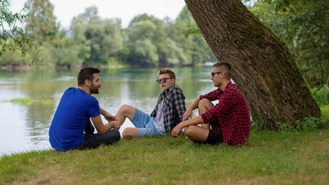 Bildet viser tre menn som sitter ute under et tre