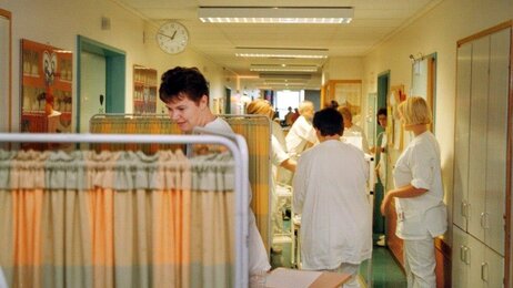 Bildet viser en sykehuskorridor med senger og mange pleiere.