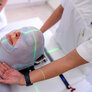 Bildet viser en pasient som skal få strpleterapi mot hodet. Vedkommende har en nettmaske på seg, og lysstriper viser hvor det skal stråles
