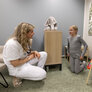 Bildet viser en sykepleier som sitter på huk foran ei jente. De er på et rom på sykehuset med en tøyelefant og et tegnestaffeli.