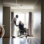 Bildet viser en sykepleier som triller en eldre mann i rullestol