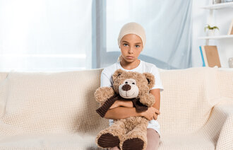 Bildet viser et sykt barn som sitter i en sofa og har en teddybjørn i fanget