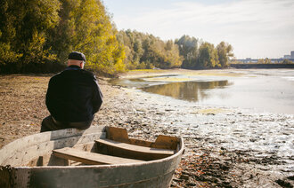 Bildet viser en mann som sitter på en båt og ser ut over en innsjø