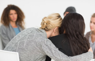 Bildet viser en terapigruppe hvor en kvinne omfavner en annen kvinne
