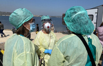 Bildet viser helsepersonell i smittevernutstyr på en strand.