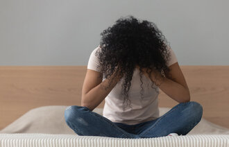 Bildet viser en kvinne som sitter alene på en seng med hodet i hendene