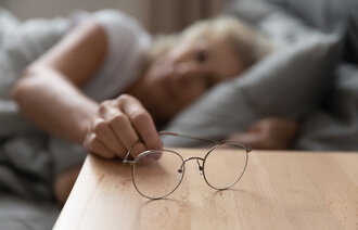 Eldre kvinne legger briller på nattbordet
