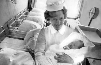 Bildet viser en jordmor anno 1976 med et nyfødt barn i armene på Ullevål sykehus