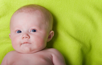 Bildet viser et nyfødt barn som ligger på et grønt teppe