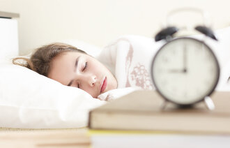 Tenåring som sover med en vekkeklokke i forgrunnen