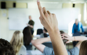 Bildet viser en hånd som rekkes opp i et klasserom.