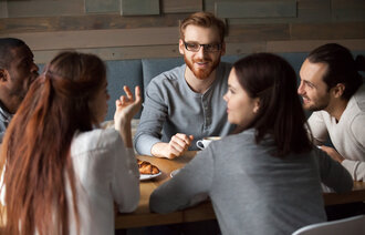 Bildet viser en gruppe unge mennesker som snakker sammen på en kafé
