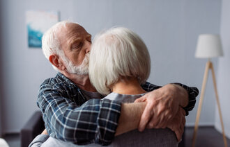 Bildet viser en eldre mann som omfavner en eldre kvinne mens han kysser henne på pannen.
