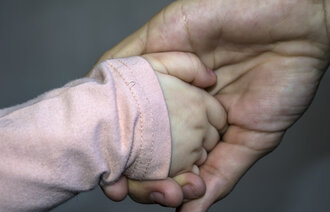 Bildet viser hånden til et lite barn i en voksen hånd