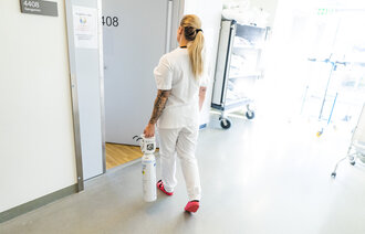 Bildet viser sykepleier med oksygenflaske på vei inn til en lungepasient på Ahus.