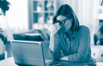 Bildet viser en dame som sitter hjemme foran en laptop. Hun ser sliten ut og tørker øynene under brillene