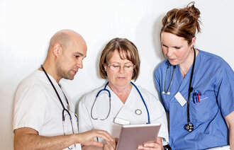 Bilde viser tre helsearbeidere som studere innhold på en Ipad.