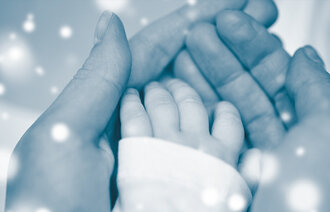 Bildet viser en mors hender som holder rundt en liten babyhånd