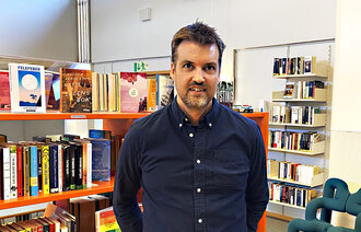 Bildet viser innleggsforfatteren foran hyller med barnebøker på et bibliotek..