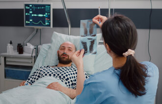 Bildet viser en pasient som ligger i sengen, og en sykepleier som ser på røntgenbilder.