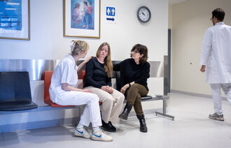 Bildet viser en ung kvinne som får trøst av pårørende og sykepleier på venteværelset. En lege går i bakgrunnen.