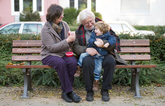 Bildet viser et eldre par og et barn som sitter på en benk