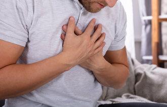 Mann med smerte i brystet holder hendene mot brystet.