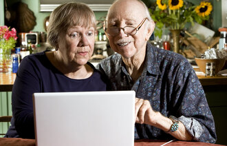 Bildet viser to eldre personer som sitter foran en laptop