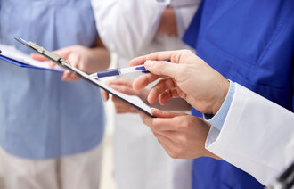 Bildet viser helsepersonell med lyseblå, mørkeblå og hvite uniformer. En av dem holder en skriveplate. Kun hendene og overkroppene synes.