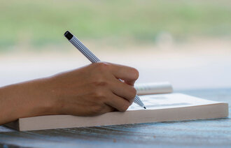 Bildet viser hånden til en som skriver dagbok. Hånden holder en penn.