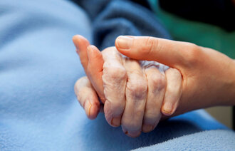Bildet viser en gammel og en ung hånd som holder hender