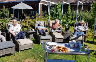 Bildet viser sykehjemsbeboere som sitter i solstoler i hagen og nyter solen. Foran står et bord med vafler.