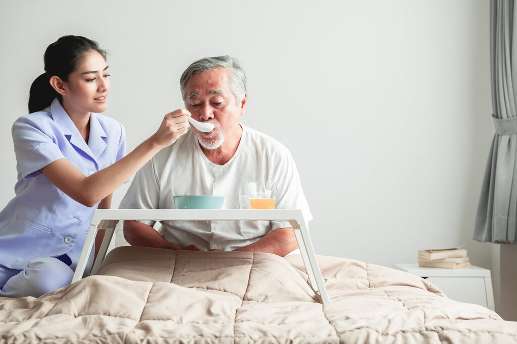 Bildet viser en japansk sykepleier som mater en eldre mann.