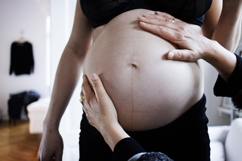 Bildet viser en gravid mage som blir undersøkt av to hender.