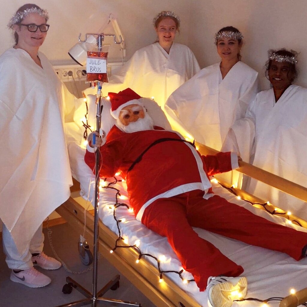 Bildet viser julenissen i en pasientseng omgitt av pleiere i Lucia-drakter.